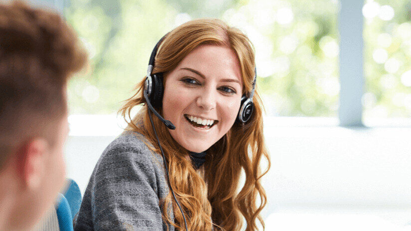 A smiling customer service adviser wearing a headset, talking with a colleague