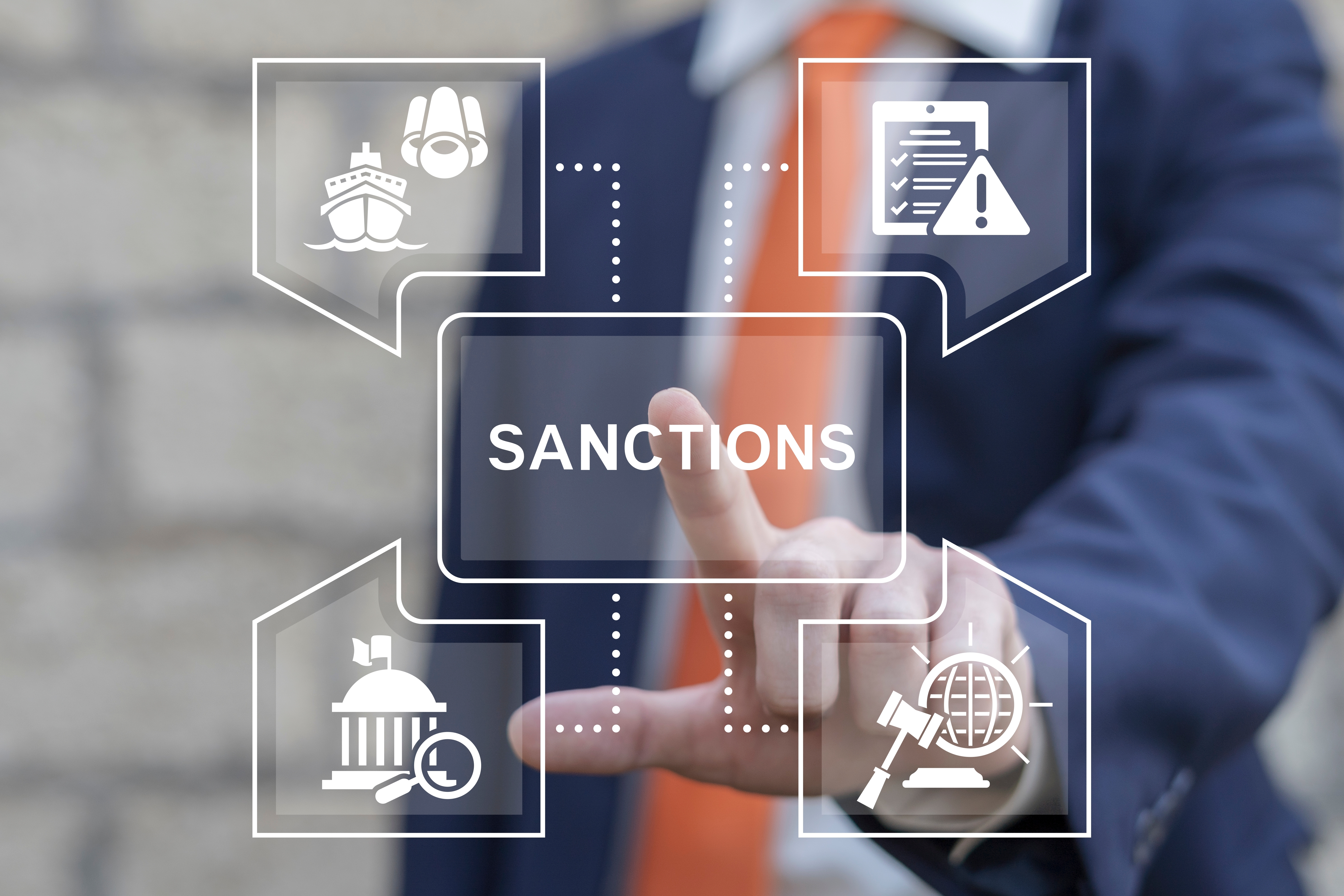 A man wearing a blue suit and red tie, pointing towards a graphic illustrating what sanctions are and the various elements related to them.